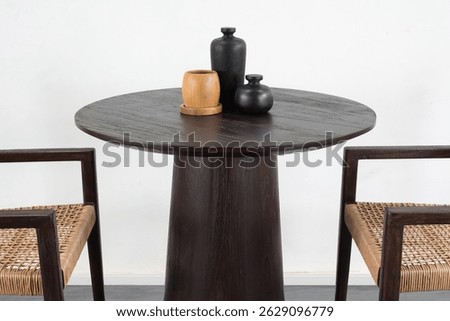 A studio shot features a round dining table made of dark-toned solid wood, possibly dark mango wood.                