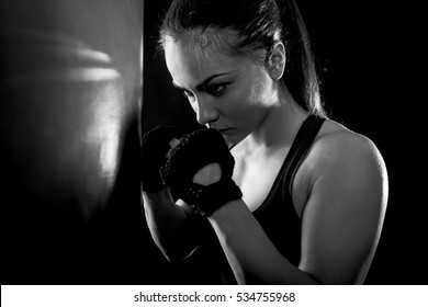 Studio Shot Of Female Boxer On The Defensive Guard Next To Boxing Bag, Black And White.