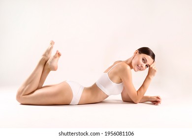 Studio shot of fit woman wearing seamless underwear in lying on the floor isolated on white. Slim attractive female with flat belly in white lingerie. Copy space, close up, background.