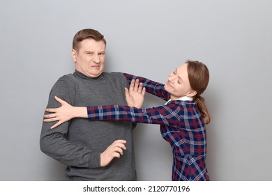 Studio shot of funny couple, happy cheerful woman is trying to hug man resisting and grimacing from displeasure, both are standing over gray background. Relationship concept, human emotions - Shutterstock ID 2120770196