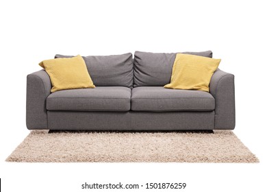 Studio shot of a grey sofa with green pillows on a carpet isolated on white background