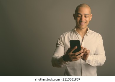 Studio shot of handsome bald businessman wearing white shirt while using mobile phone against gray background - Shutterstock ID 2113381937