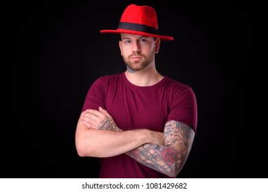 Studio Shot Of Handsome Bearded Man Wearing Red Fedora Hat Against Black Background