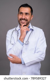 Studio shot of handsome bearded Persian man doctor against gray background