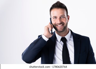 Studio shot of handsome businessman wearing suit while standing at isolated white background and talking with somebody on his mobile phone. 