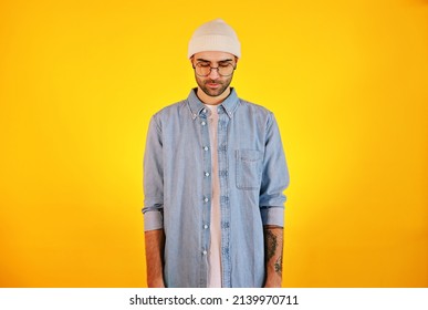 Studio Shot Of  Handsome Man In Jeans , Glasses And White Hat On Yellow Background. Thinking Concept. Tatoo And Beard. 