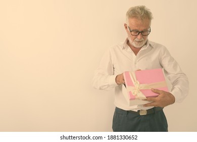 Studio Shot Of Handsome Senior Bearded Man Opening Gift Box With Eyeglasses Against White Background