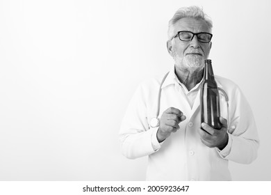 Studio Shot Of Handsome Senior Bearded Man Doctor Against White Background In Black And White