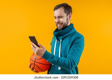 Studio shot of handsome smiling bearded young man holding basketball ball in hand, watching play live broadcast online and making bets at favourite team using bookmaker's mobile application. - Powered by Shutterstock