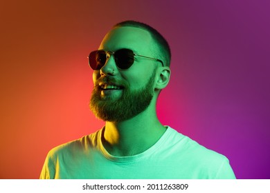 Studio shot handsome smiling caucasian young man in stylish sunglasses isolated gradient orange pink background in neon light  Copyspace for ad
