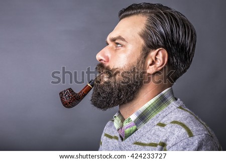 Studio shot of a handsome young man with retro look smoking pipe over gray background