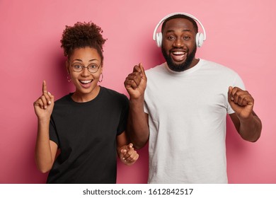 Studio Shot Of Happy Black Woman And Man Dance With Rhythm Of Music, Have Glad Expressions, Spend Free Time At Disco Party. Curly Afro American Woman Has Fun With Professional Male Dj. Loud Sound