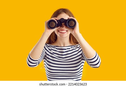 Studio shot of happy cheerful beautiful young woman in casual striped top standing isolated on yellow color background, holding modern binoculars, looking in distance and smiling - Powered by Shutterstock