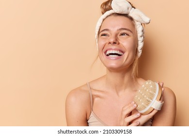 Studio Shot Of Happy European Woman Smiles Brooadly With White Teeth Holds Dry Brush For Body Scrubbing Feels Very Glad Poses Against Brown Background Blank Space For Your Promotional Content