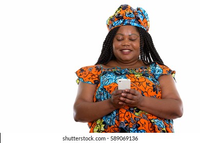 Studio Shot Of Happy Fat Black African Woman Smiling While Wearing Traditional Clothes And Using Mobile Phone