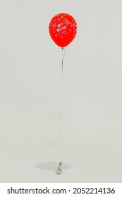 Studio Shot Of Happy New Year Festival Celebration Party Floating Helium Inflatable Firework Confetti And Star Pattern Red Balloon Flying With String Weighted On Small Sandbag On White Background.