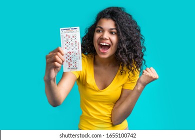 Studio Shot Of Happy Smiling African Girl Holding Lottery Ticket In One Hand And Showing 