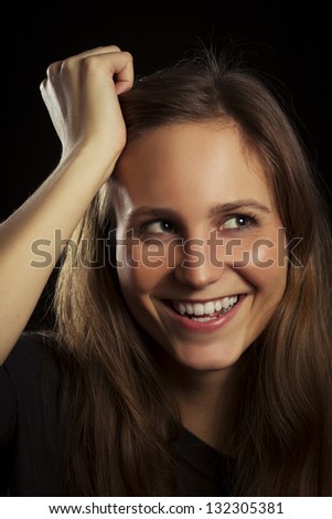 Studio shot of a happy young woman / girl with lowkey lighting. Black background.