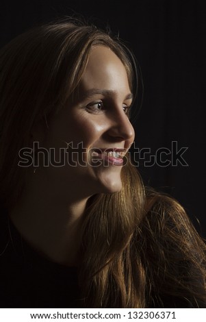 Studio shot of a happy young woman / girl with lowkey lighting. Black background.