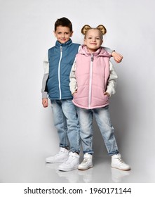 Studio shot of little brother with sister in warm outerwear blue and pink vests, jeans, sneakers and sweatshirt posing for the camera, isolated on white. Advertising of children's fashion clothes