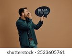 Studio shot of a man announcing Black Friday sale while holding speech bubble against neutral background. Copy space.