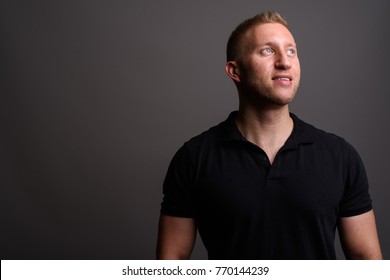 Studio Shot Of Man With Blond Hair Wearing Black Polo Shirt Against Gray Background