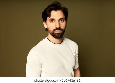 Studio shot of manly photogenic sporty athletic man fitness trainer with stylish haircut and beard, standing against brown background looking at camera with confident serious facial expression - Shutterstock ID 2267416491