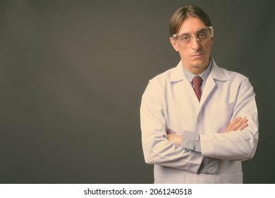 Studio Shot Of Mature Handsome Italian Man Doctor Wearing Protective Glasses Against Gray Background