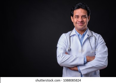 Studio Shot Of Mature Indian Man Doctor Against Black Background