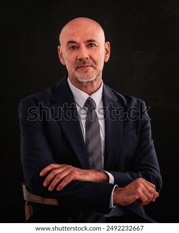 Studio shot of a mid aged man wearing suit and sitting against isolated dark background. Copy spacee.