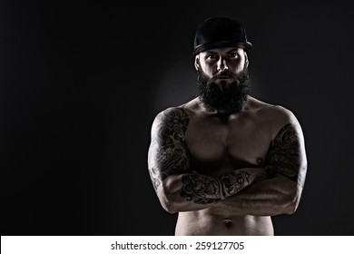 Studio Shot Of Muscular Man With Tattoo  And  Baseball Cap On Dark Background