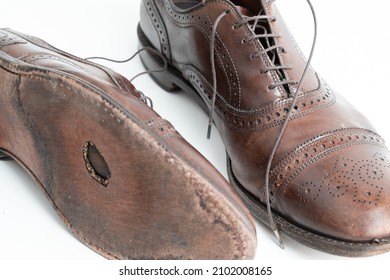Studio shot of old, weary and little scratched cap toe lace op oxford shoes in burnished brown color, on white background. Hole in the sole of the right shoe. Old shoes that need repair. - Shutterstock ID 2102008165