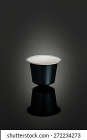 Studio shot on a black reflecting surface of a single blue coffee pod, facing up