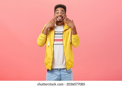 Studio shot of pleased and impressed good-looking stylish young african american being delighted with result after facial skin message smiling broadly touching face posing over pink background - Shutterstock ID 2036077085