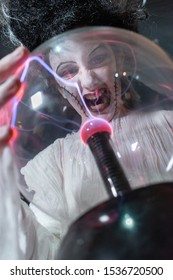 Studio Shot Portrait Of Young Girl In Costume Dressed As A Halloween, Cosplay Of Scary Bride Of Frankenstein Posing With Glass Lightning Ball