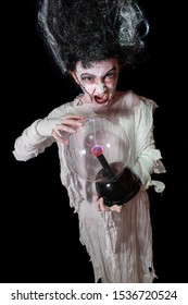 Studio Shot Portrait Of Young Girl In Costume Dressed As A Halloween, Cosplay Of Scary Bride Of Frankenstein Posing With Glass Lightning Ball