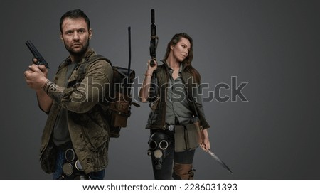 Studio shot of post apocalyptic couple survivors with guns against gray background.
