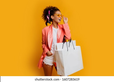 Studio Shot Of Pretty Black Woman With White Shopping Bag Standing Over Yellow Background. Trendy Spring Fashionable Look.