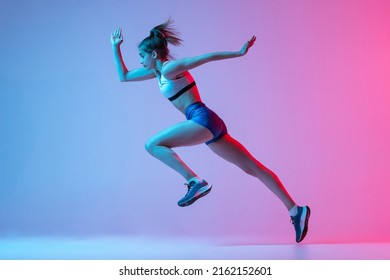 Studio Shot Of Professional Female Athlete, Runner Training Isolated On Pink Studio Background With Blue Neon Filter, Light. Concept Of Action, Motion, Speed, Healthy Lifestyle. Copy Space