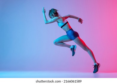 Studio Shot Of Professional Female Athlete, Runner Training Isolated On Pink Studio Background With Blue Neon Filter, Light. Concept Of Action, Motion, Speed, Healthy Lifestyle. Copy Space