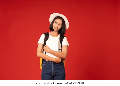 Studio shot of red background of short hair Asian female international university student wearing casual clothes and hat, holding books, shoulder bag, knowledgeable and future of the nation. - Powered by Shutterstock