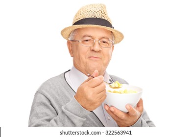 Studio Shot Of A Senior Gentleman Eating Cereal From A Bowl And Looking At The Camera Isolated On White Background