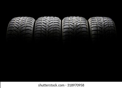 Studio shot of a set of four black car tires lined up horizontally in a dark ambient on black background