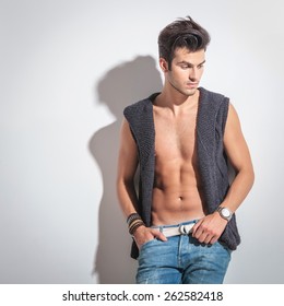 Studio shot of a sexy young fashion man looking down while holding one hand in his pocket.