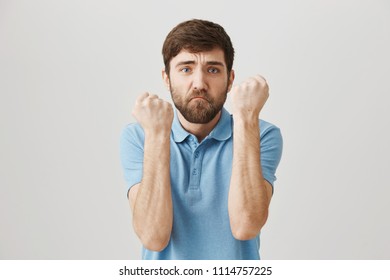 Studio Shot Of Silly European Guy Being Afraid While In Middle Of Fight, Raising Fists, Trying To Protect Himself From Being Bitten, Standing Over Gray Background.