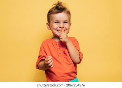 Studio shot of a smiling boy eating fresh carrots on a yellow background. The concept of healthy baby food, carotene. - Powered by Shutterstock