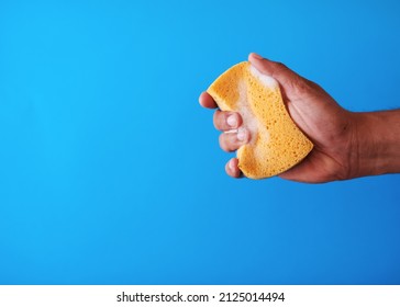 A studio shot of a soapy sponge being squeezed on a blue background