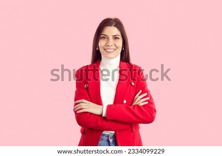 Studio shot of stylish businesswoman in smart casual outfit. Happy beautiful young business woman in red suit jacket, jeans and white turtleneck standing isolated on pink background. Fashion concept