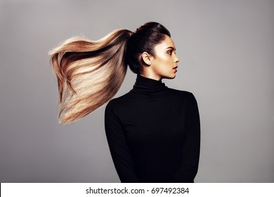 Studio Shot Of Stylish Young Woman With Flying Hair Against Grey Background. Female Fashion Model With Long Hair.