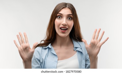 Studio shot of surprised Young female with long chestnut hair, dressed in casual clothes, smiling happily and raises her hands. Surprise. Human emotions, facial expression concept. - Shutterstock ID 1827970580